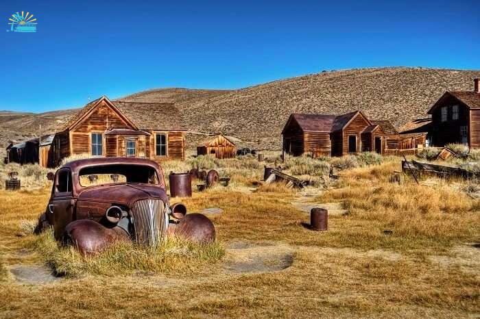 A photo capturing an old car and ruins of the houses in the abandoned town of Bodie in California
