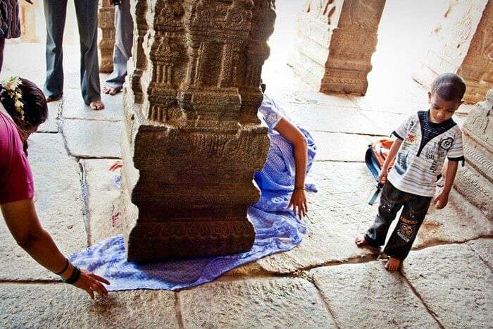 People passing objects under the hanging pillar at Lepakshi