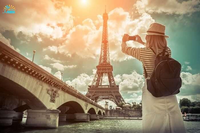 Woman tourist taking a selfie near the Eiffel tower in Paris under sunlight and blue sky
